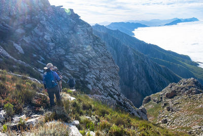 Hikers with backpack trekking down steep hill with clouds and mountain ranges in sight 