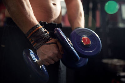 Midsection of shirtless man lifting dumbbells