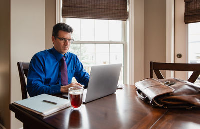 Man in shirt and tie working from home using computer at dining table.