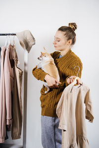 Woman holding dog with garment standing against wall