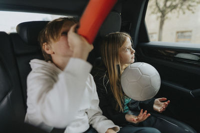 Boy drinking water while sitting with sister in car during weekend trip