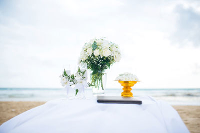 Close-up of white flowers and wineglasses on table at beach