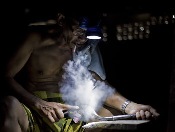 Shirtless manual worker smoking cigarette while working at night