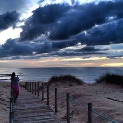 Silhouette of people standing on beach against cloudy sky