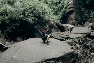 Full length of young man kneeling on rock in forest
