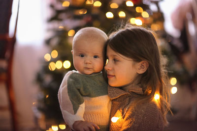 Baby and her older sister on the background of the christmas tree, the concept of christmas