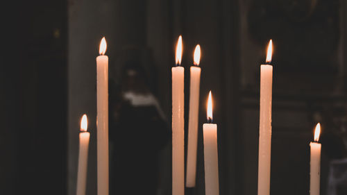 Close-up of illuminated candles burning in temple with a nun in the background 