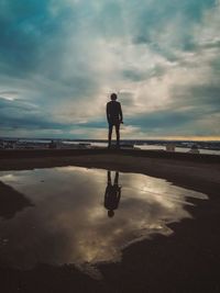 Rear view of man standing on rooftop against cloudy sky during sunset