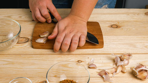 Close-up of a woman's hands on a cutting board crushing garlic cloves with a large knife