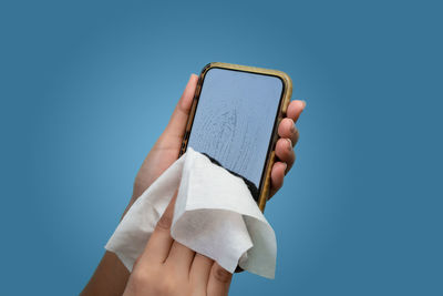 Close-up of hand holding smart phone against blue background