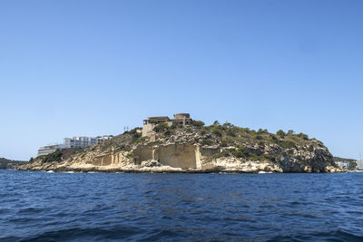 Building by sea against clear blue sky