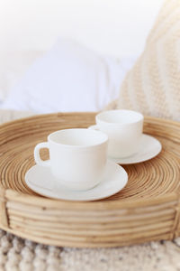 Wicker tray with white cups on a cozy bed with pillows