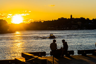 Rear view of silhouette people on sea against sky during sunset