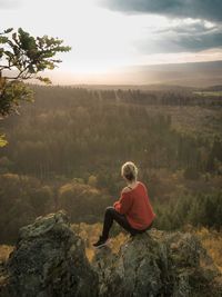 Rear view of woman sitting on rock against sky during sunset