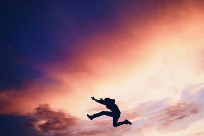 Side view of silhouette person jumping in mid-air against orange sky