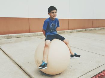 Full length of smiling boy sitting on large ball outdoors