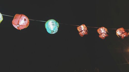 Low angle view of illuminated lanterns hanging against black background