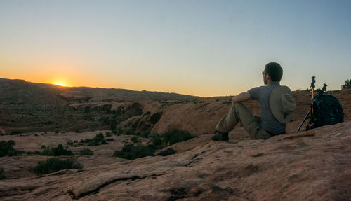 Rear view of man sitting on land against sky during sunset