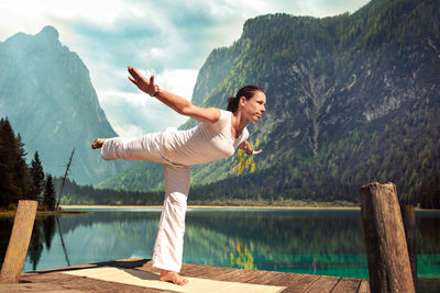 Mid adult woman exercising on pier over lake against mountains