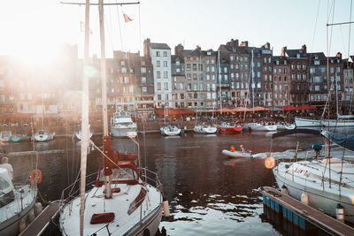 Sailboats moored on canal amidst buildings in city against sky