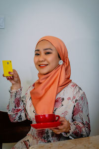 Portrait of a smiling young woman standing against wall