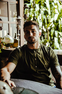 Portrait of young man sitting by plant indoors