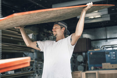 Carpenter carrying wooden plank at workshop