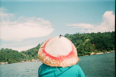 Rear view of woman in hat by lake against sky