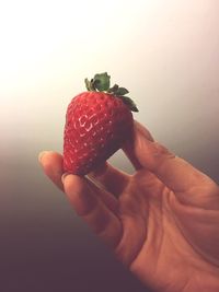 Close-up of hand holding strawberry against white background