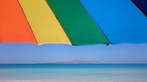 Multi colored parasol by sea against sky