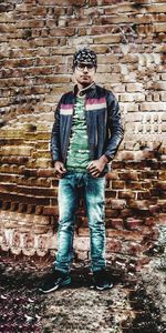 Portrait of young man standing against brick wall