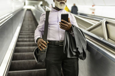 Senior businessman with suit and mobile phone carrying laptop bag on escalator