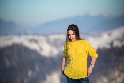 Young beautiful woman wearing yellow sweater standing against snowcapped mountain
