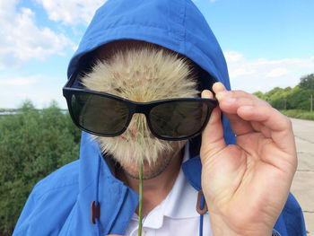 Man wearing sunglasses while covering face with dandelion