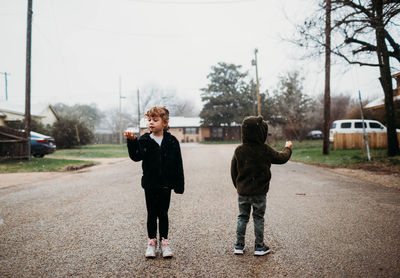 Young brother and sister standing in street catching snow flakes