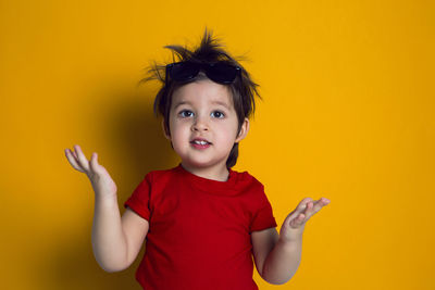 Cheerful baby boy in red t-shirt stands on yellow background
