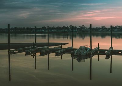 Wooden posts in lake against sky at sunset