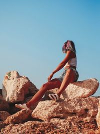 Side view of woman on rock against clear sky