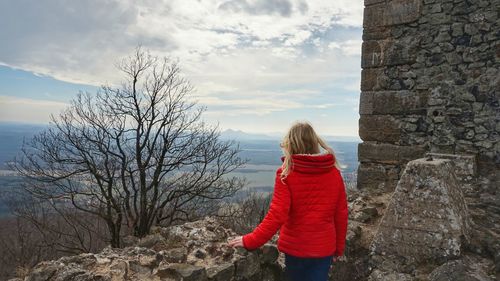 Rear view of woman standing by stone wall against sky