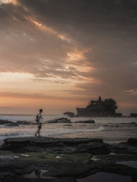 Full length of young man standing on rock looking at sea during sunset