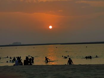 Silhouette people on beach against sky during sunset