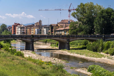 Bridge over river by buildings against sky