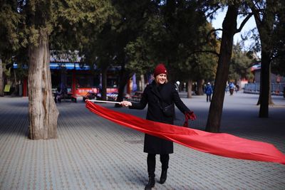 Smiling young woman with red fabric while walking on street during winter