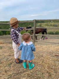 Rear view of boy standing on field.brother and sister field with horses