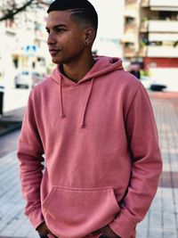 Young man looking away while standing in city