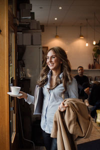 Happy young woman walking with coffee cup and overcoat at cafe