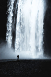 Rear view of silhouette person standing against waterfall