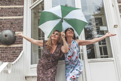 Couple of two attractive fifty year old women with umbrella in front of french villa on a rainy day