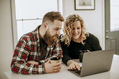 Young heterosexual couple sits at table looking at laptop computer