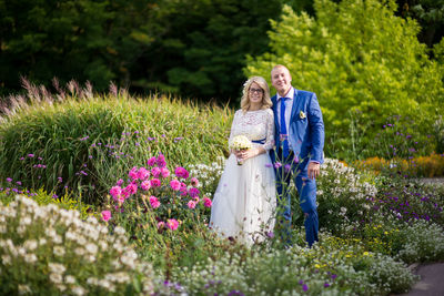 Portrait of bridal couple standing amidst flowers blooming at park